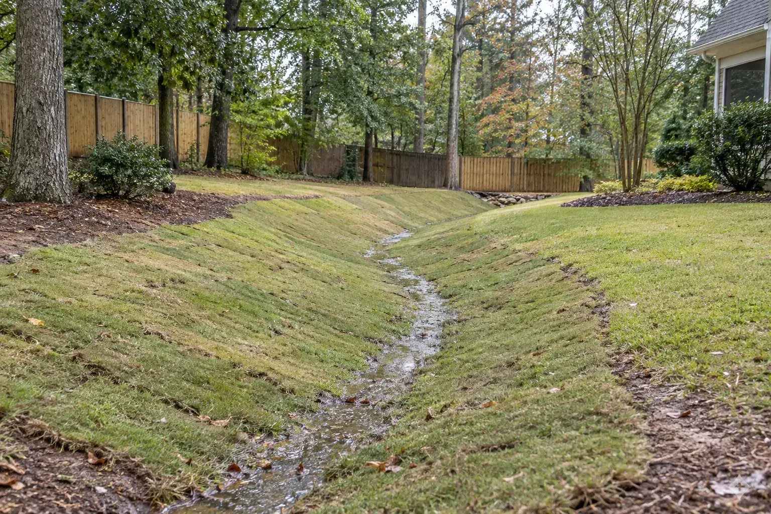Newly shaped grass drainage swale carrying light runoff through a Greer yard